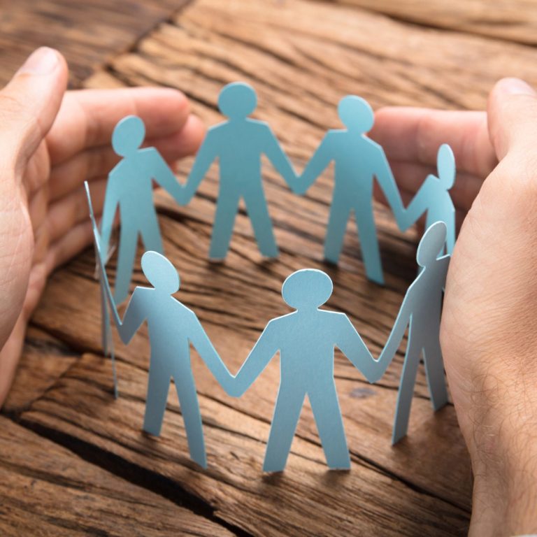 Teamcoaching und Teamentwicklung Team halten sich an den Händen, umgeben von Händen, die ihnen Halt geben.