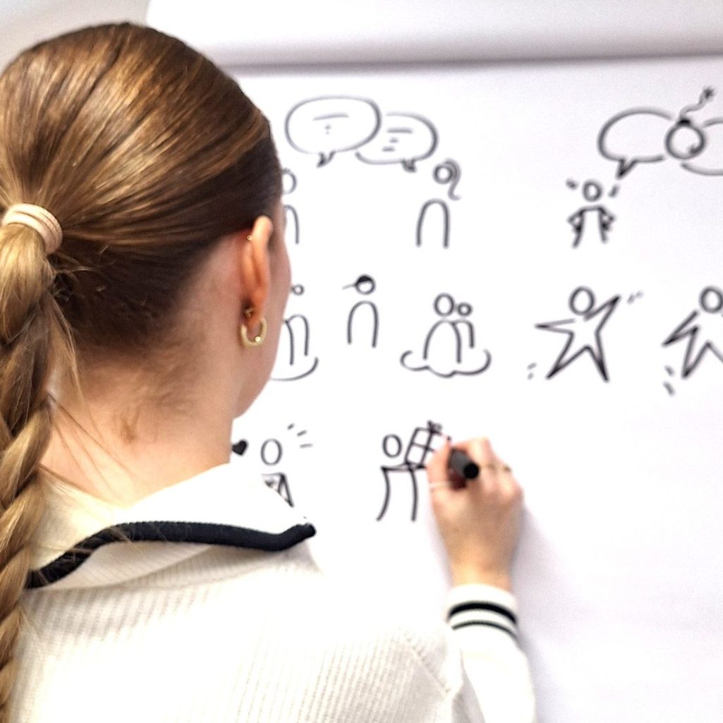 Figuren am Flipchart Frau mit Zopf zeichnet einfache Figuren auf ein Flipchart.